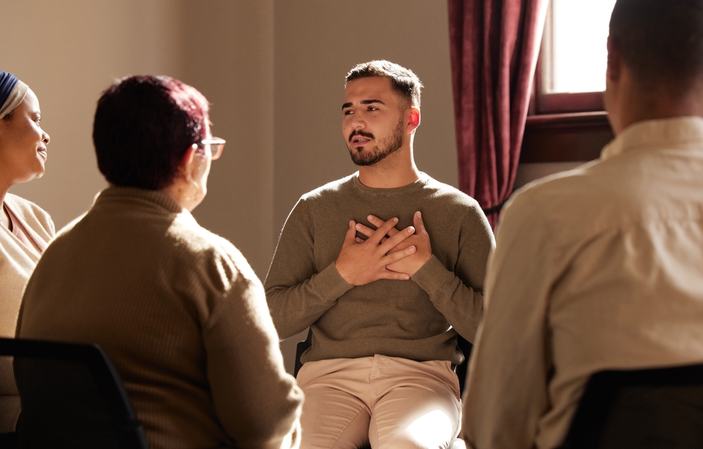 A man sat in a therapy group with his hands over his heart