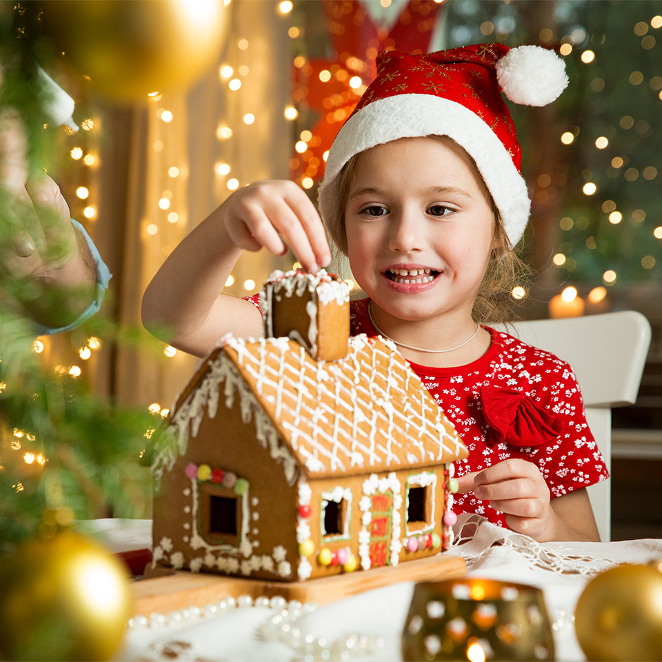Young girl in a Santa hat building a gingerbread house