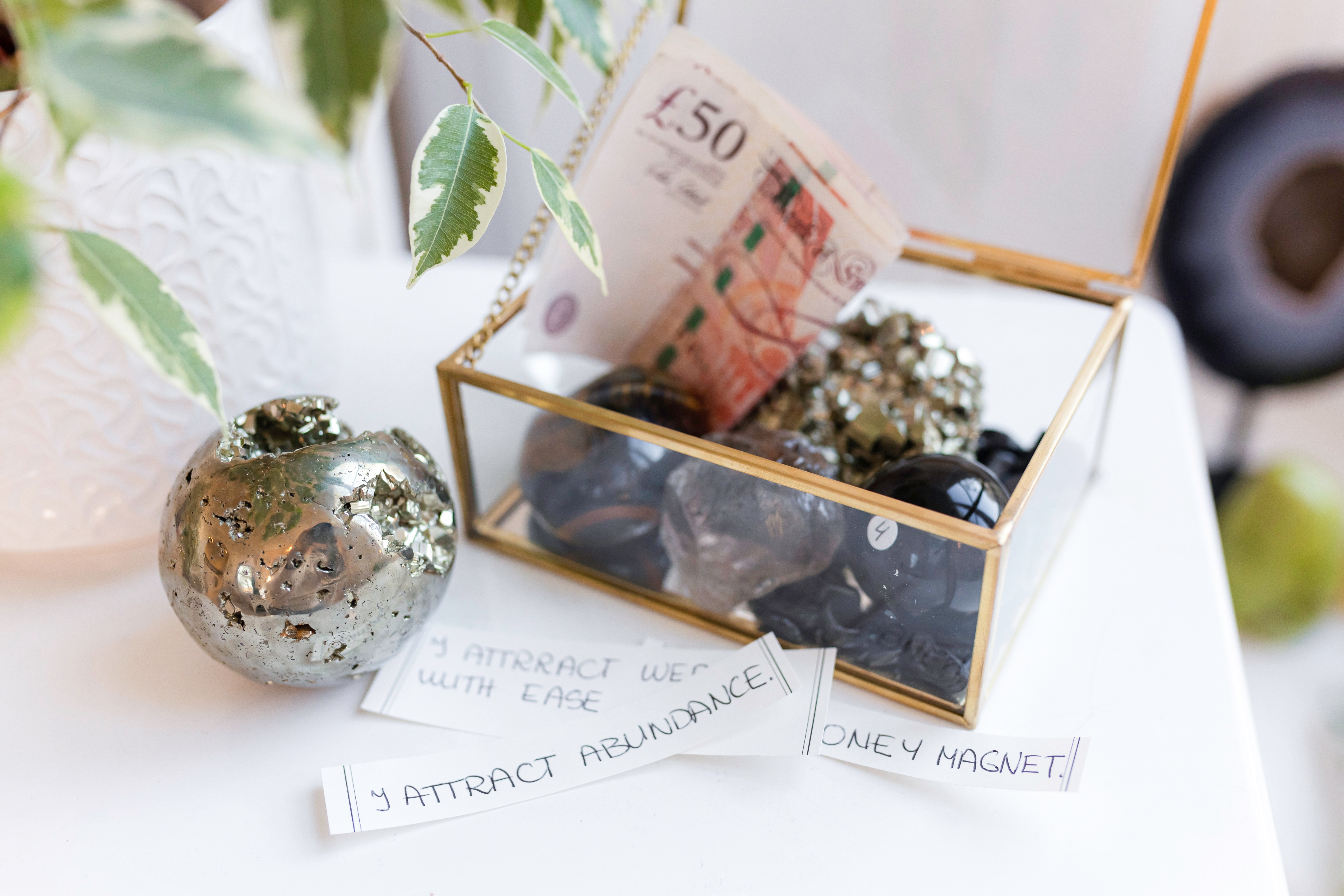 A box of crystals, with a £50 note, and some notes with writing on; two of the notes are partially obstructed but one says 'I Attract Abundance'.