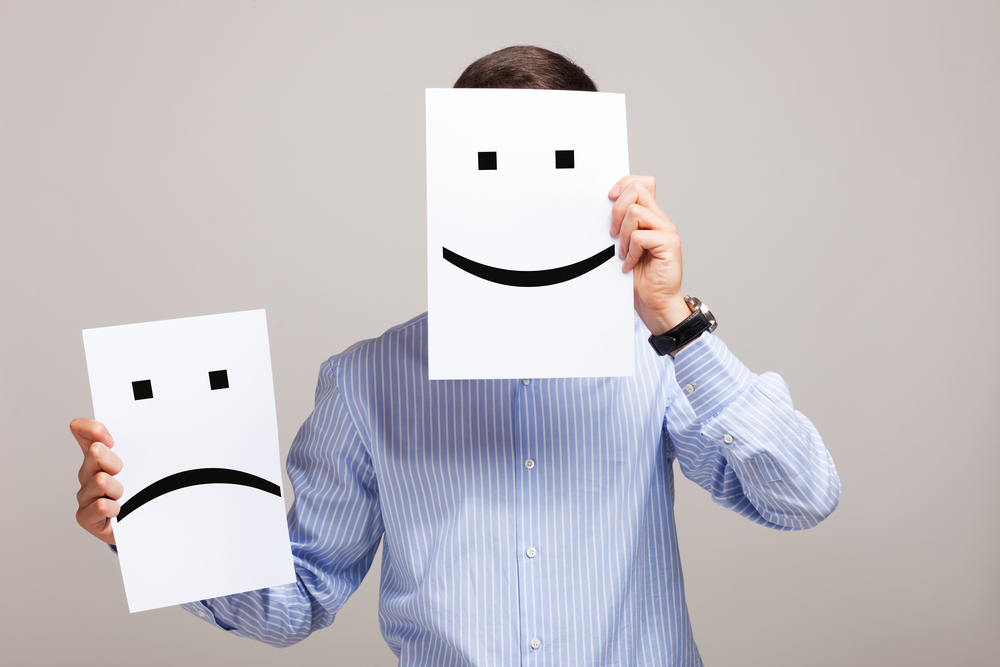 Man holding a piece of paper with a smiley face over his face and a sad face in the other hand