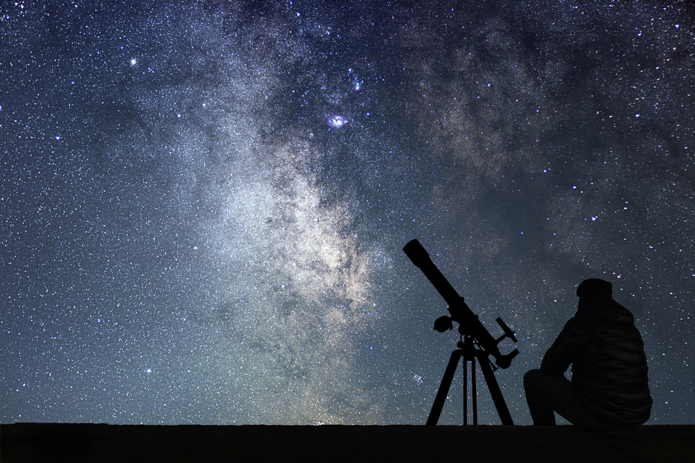 Silhouette of someone stargazing with a telescope