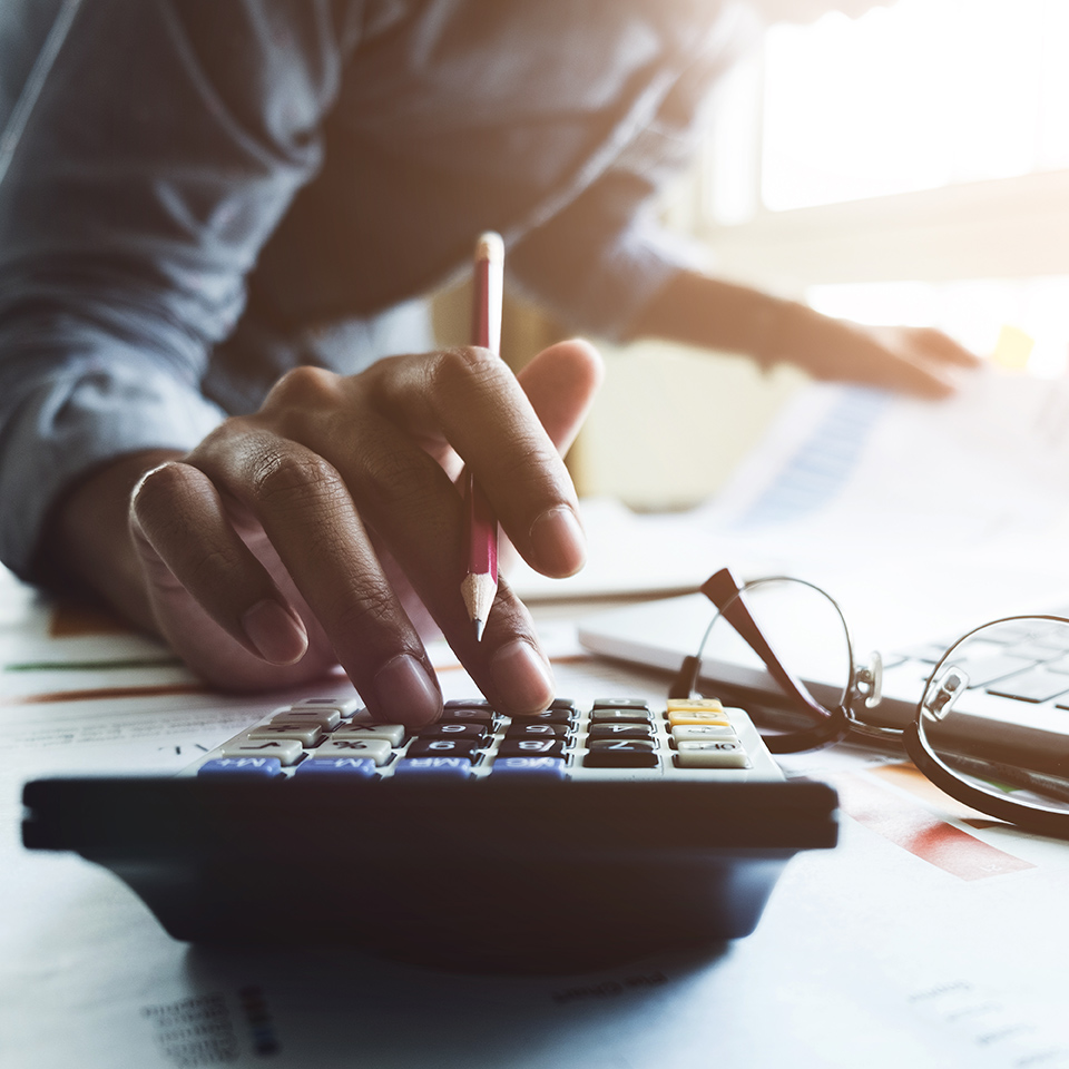 Close up of an accountant's hand holding a pen and working on a calculator