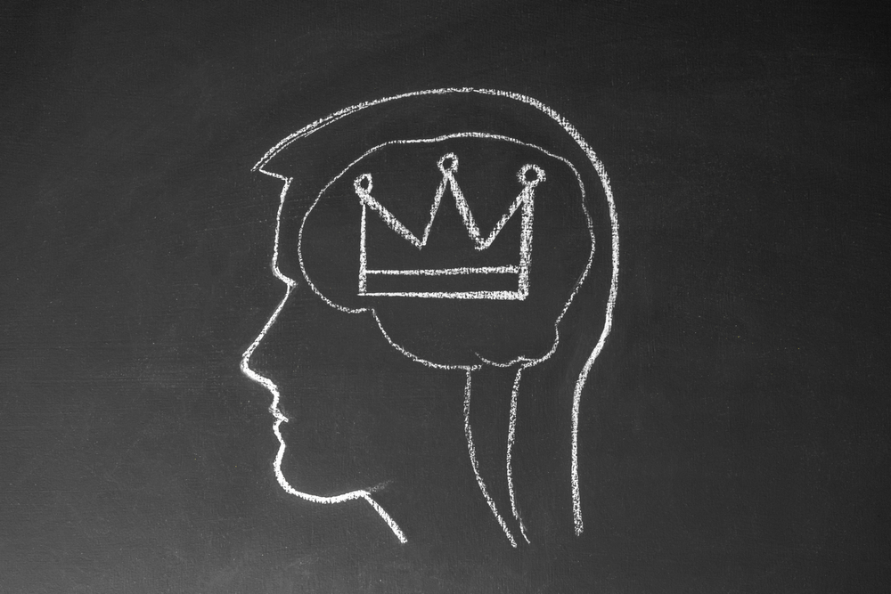 The outline of a head on a chalkboard with a crown drawn inside the brain