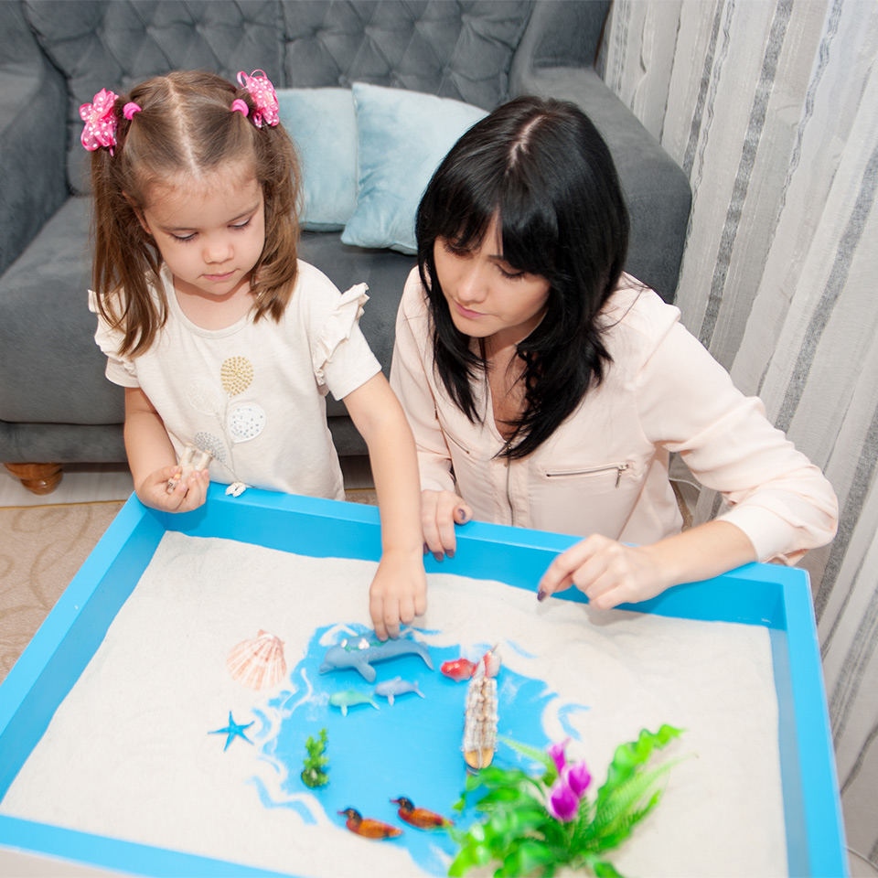 A child in sand tray therapy accompanied by a therapist