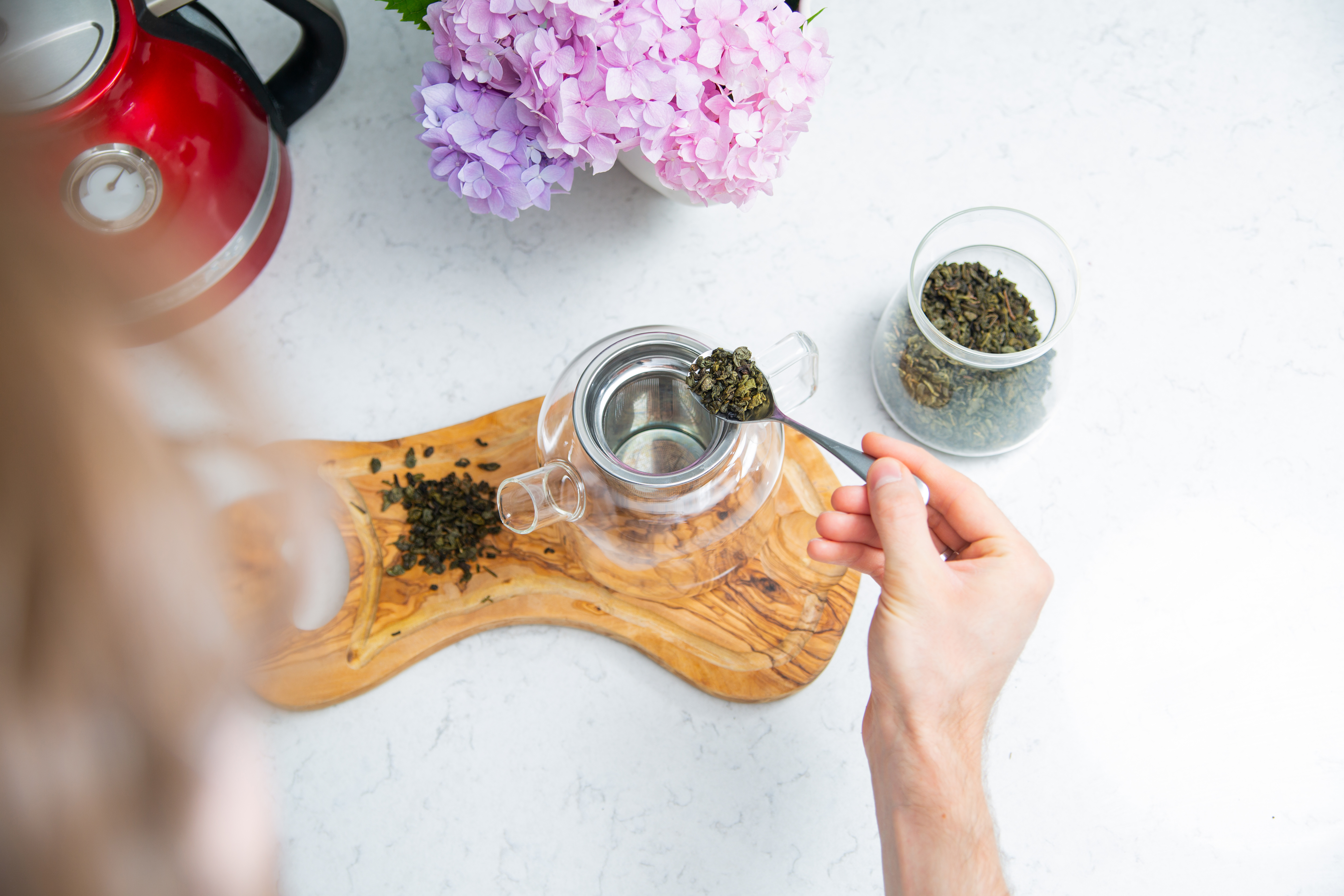 Tea leaves being put into a glass teapot