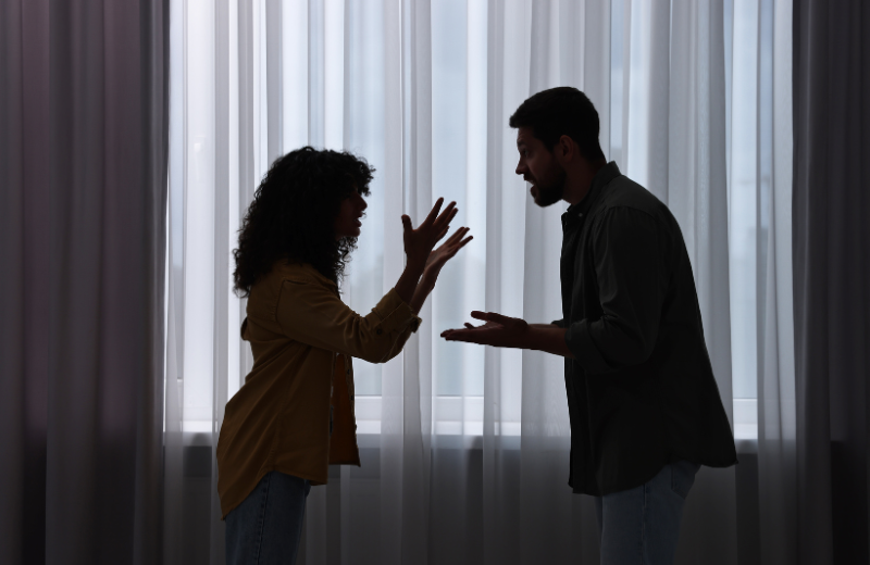 Couple arguing silhouetted against window