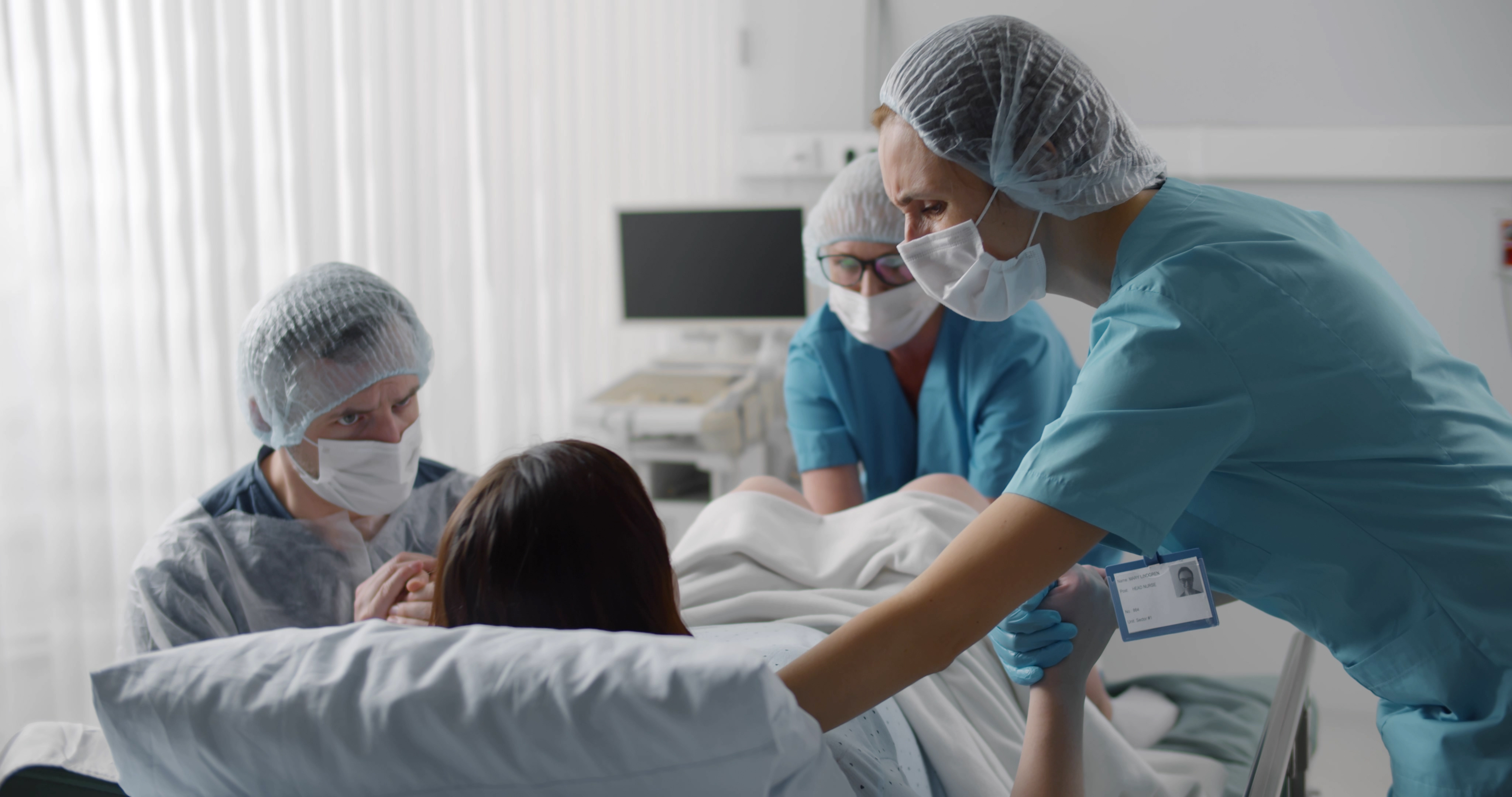 A picture of someone in a hospital giving birth with two medical professionals and their birthing partner with them