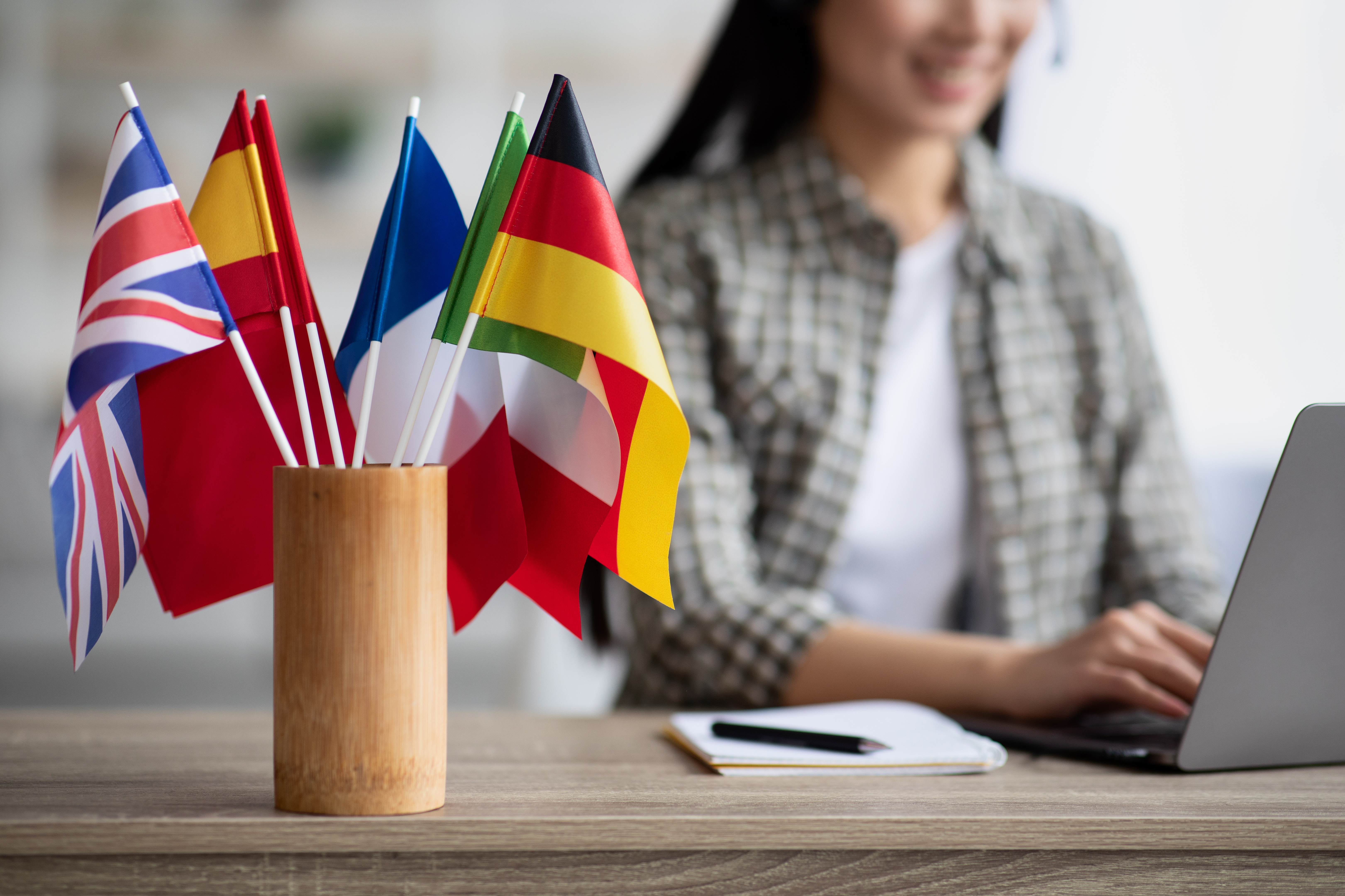 Woman on laptop learning a new language with language flags in pot