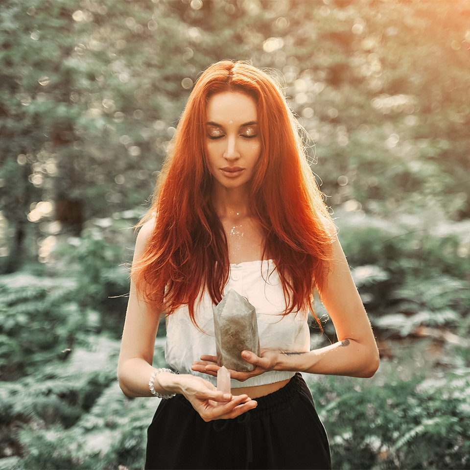 Woman in a forest practising crystal magic with a pink quartz crystal