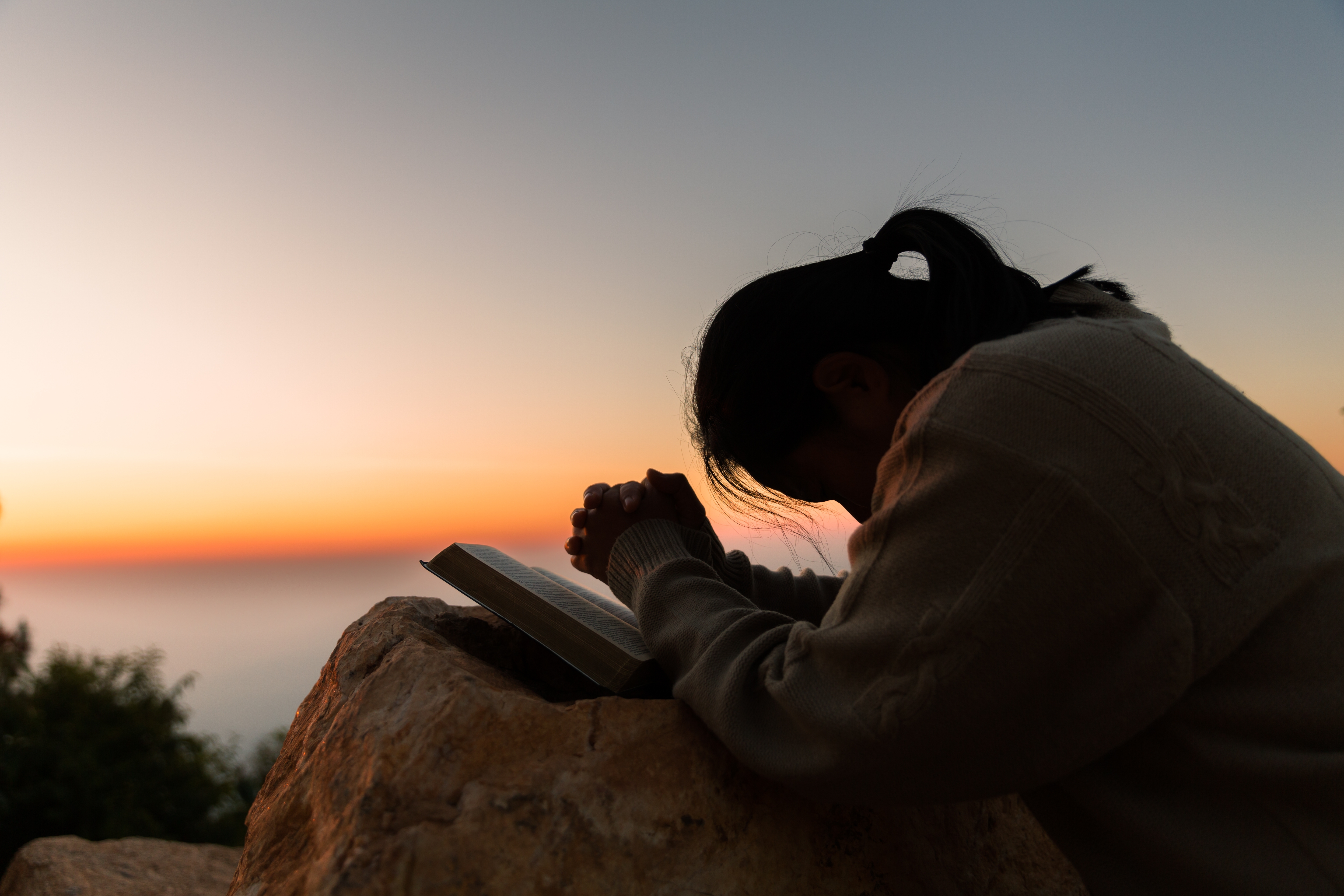 A woman praying in front of a sunset