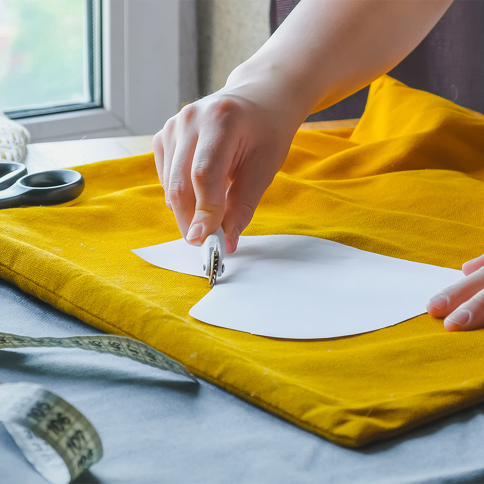 A hand holding a template over a piece of material as part of the upcycling process