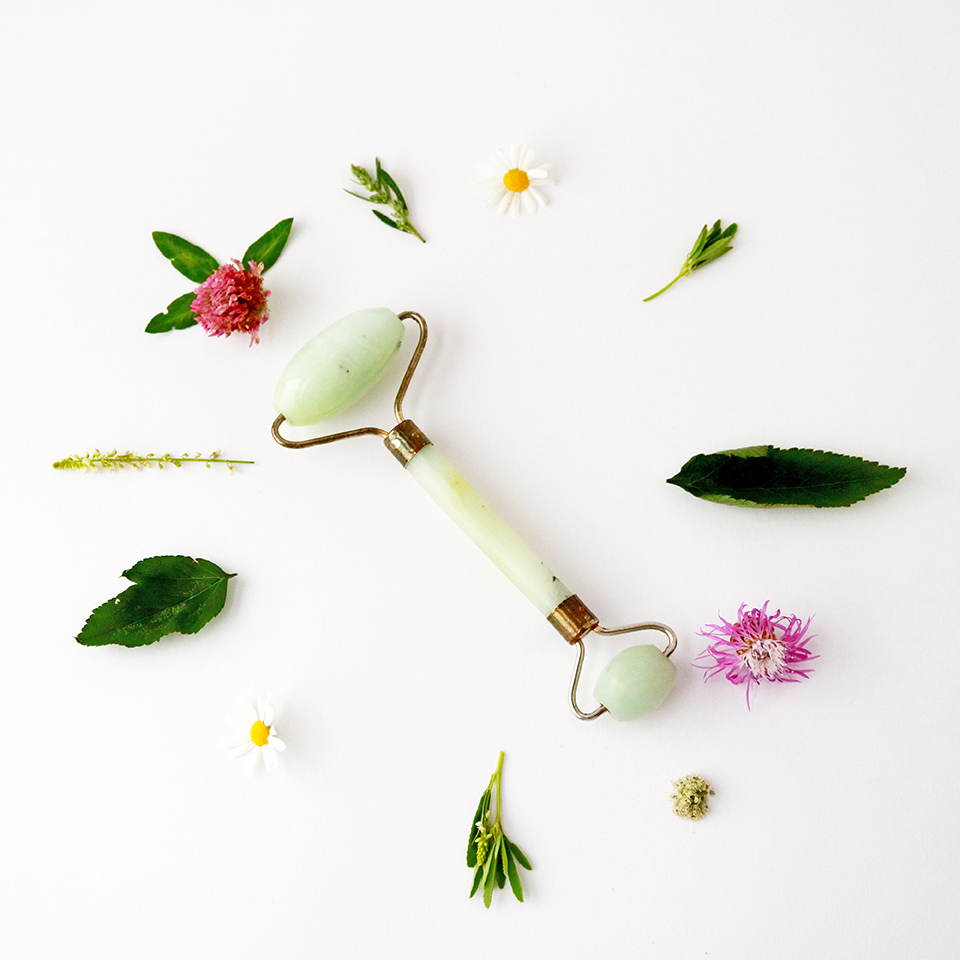 A jade roller massage tool surrounded by flowers and leaves
