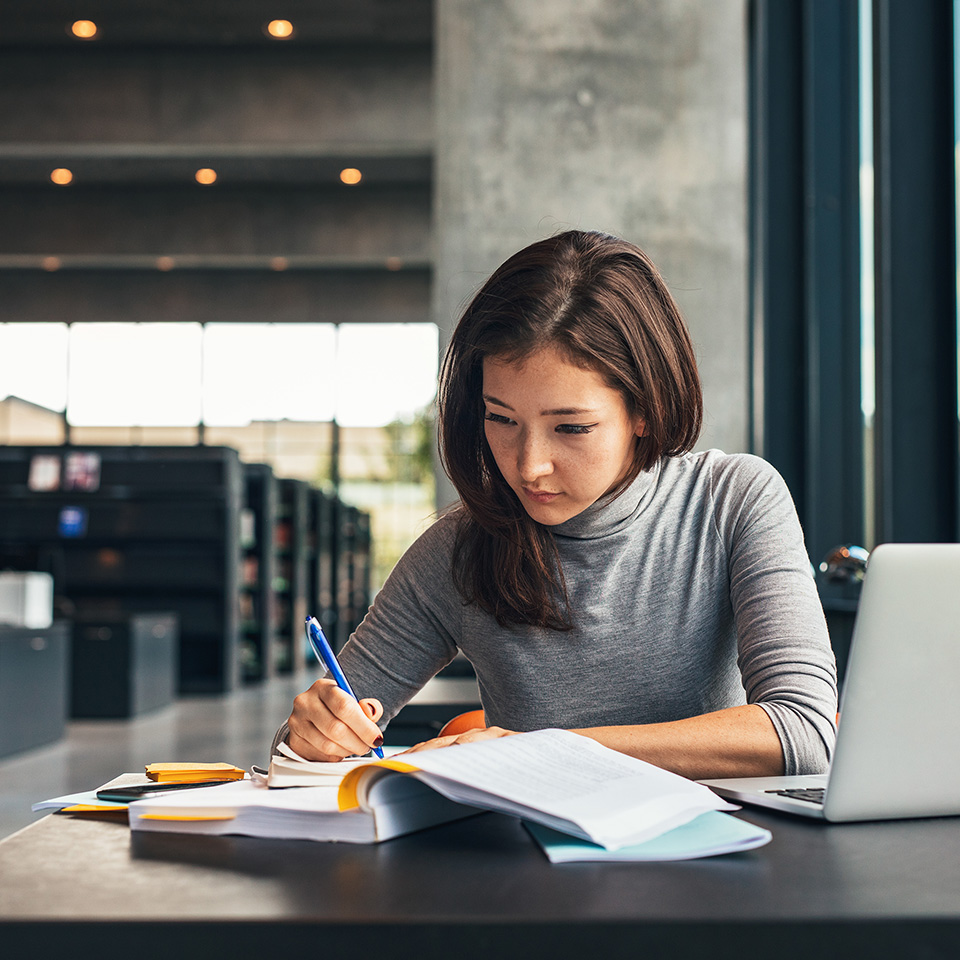 A student making notes from a book at a library