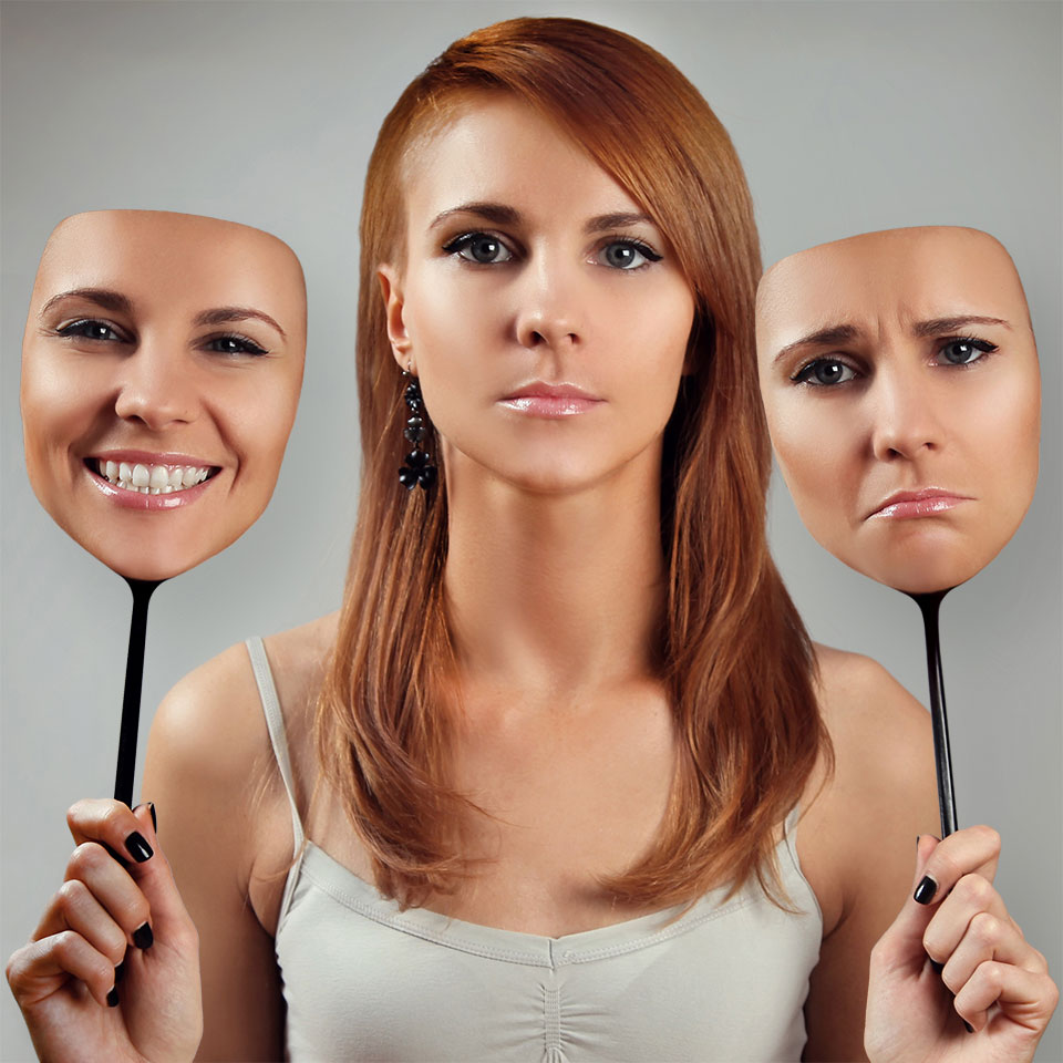 Young expressionless woman with holding up two faces - one with happy expression, one with a unhappy expression.