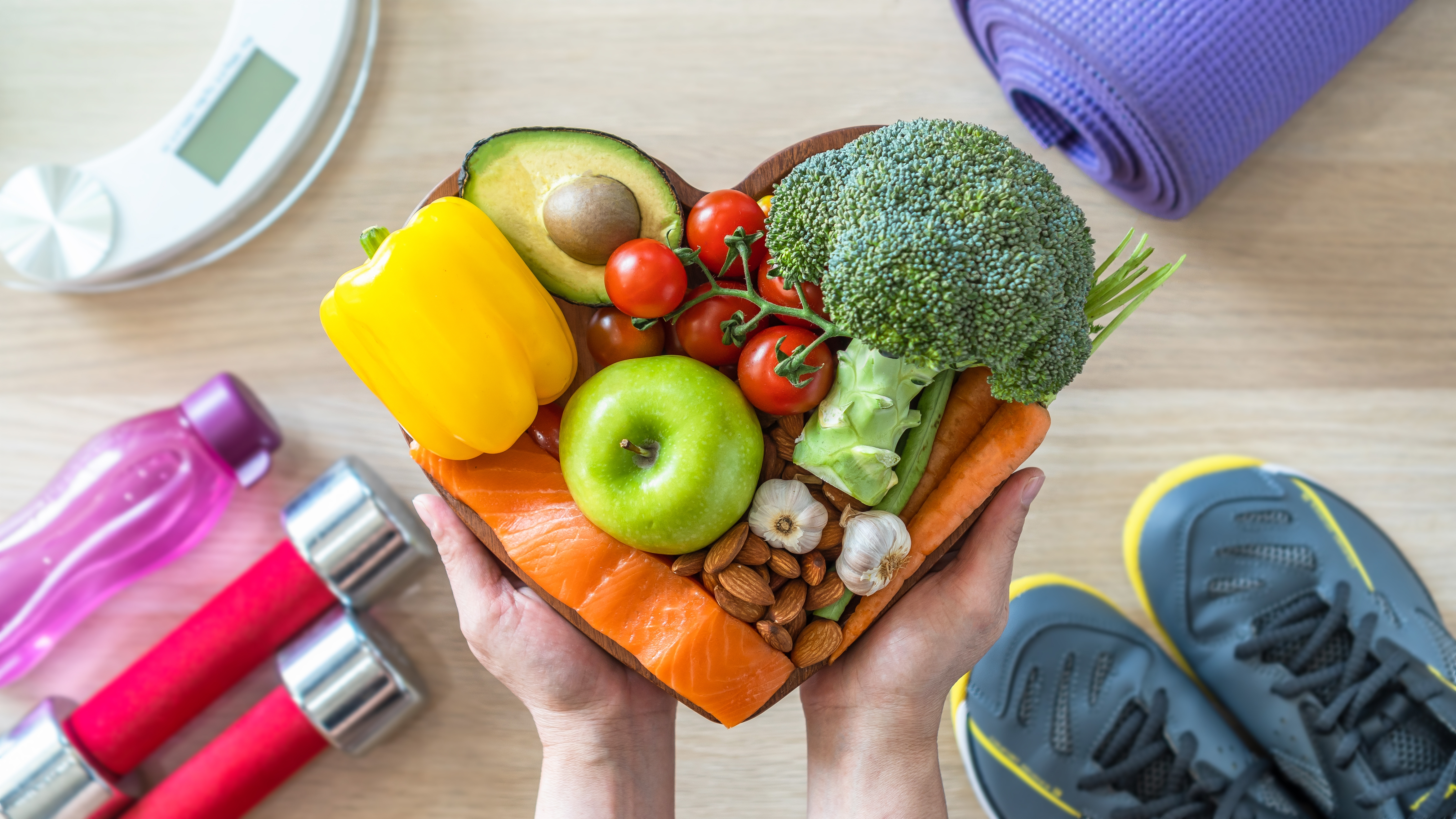 A heart shaped plate of fruit and vegetables with workout equipment in the background