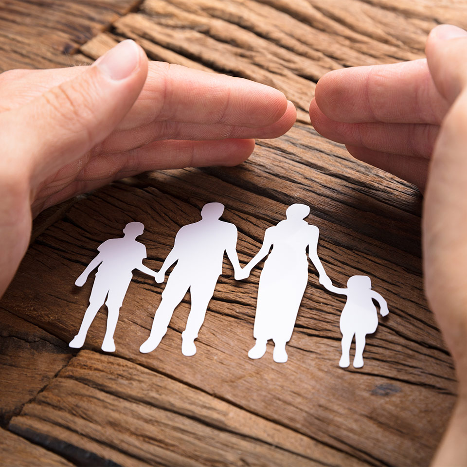 Hands protectively covering a paper cutout of a family on a wooden table
