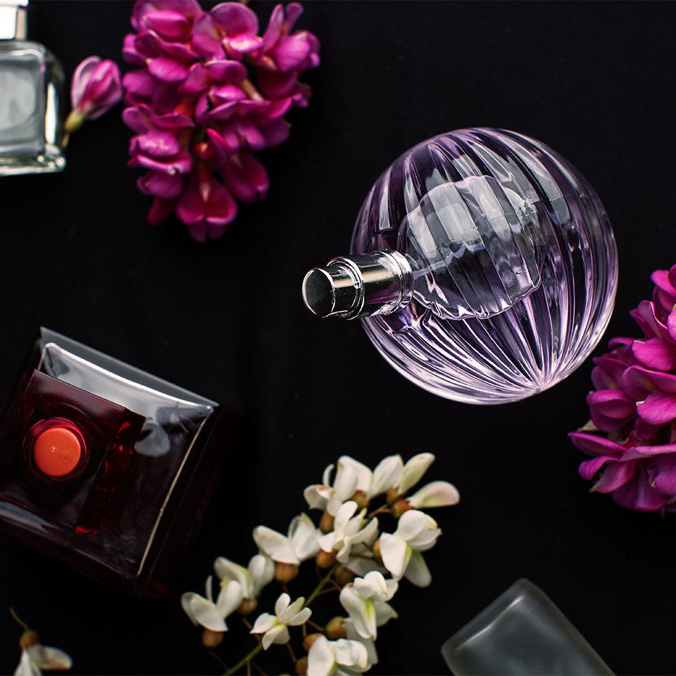 A collection of perfume bottles falling alongside flowers on a black background