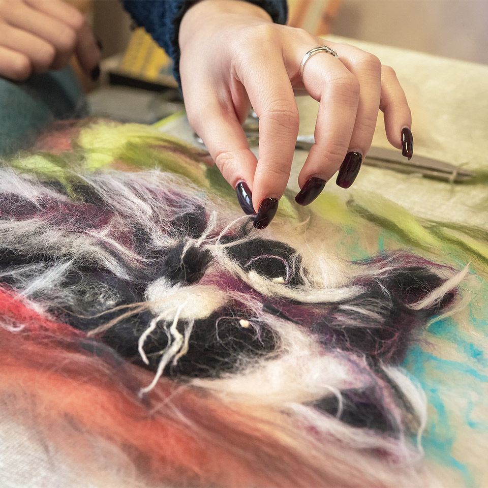 A hand working on a wet felting picture of an animal