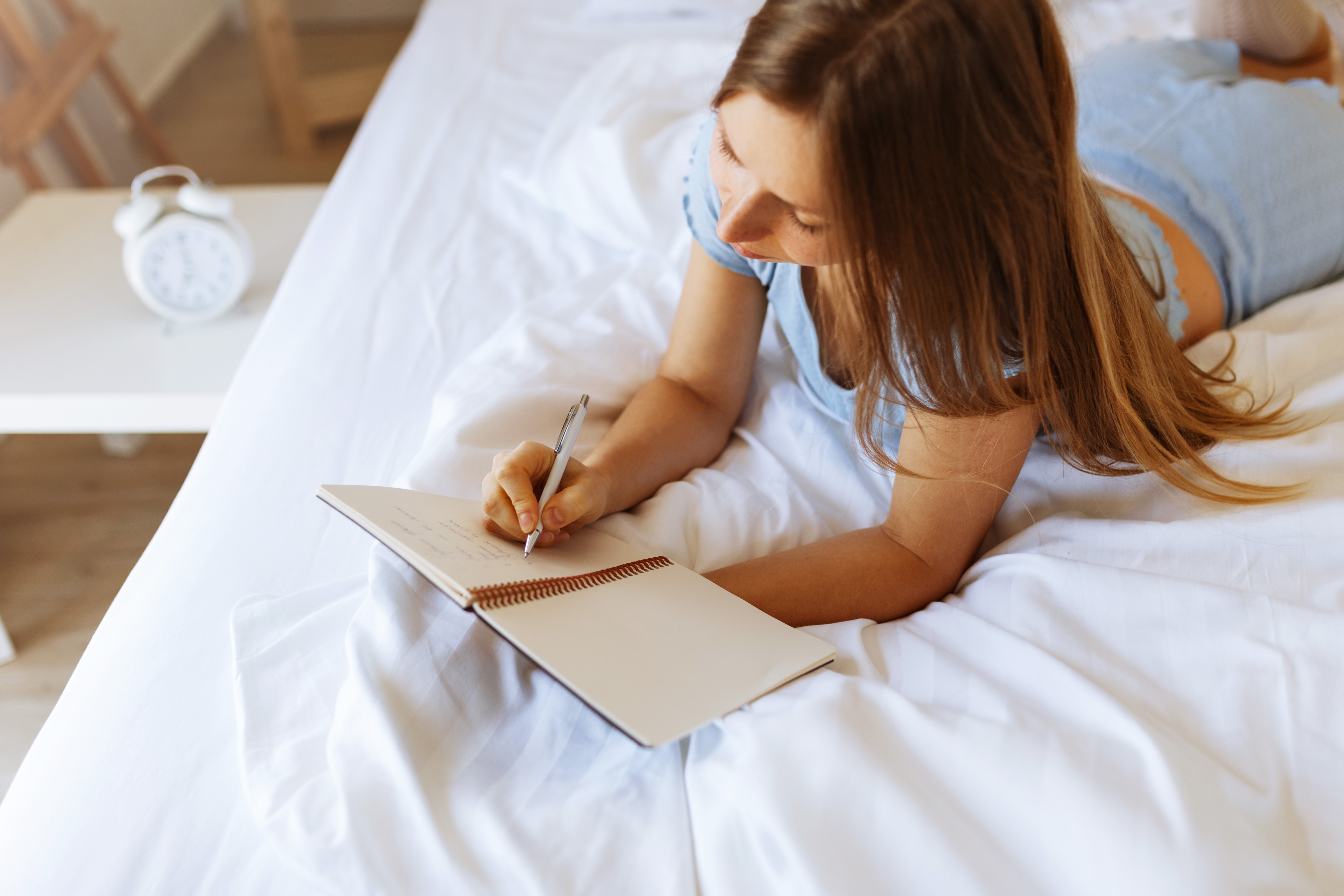 A woman lying on a bed writing in a notebook