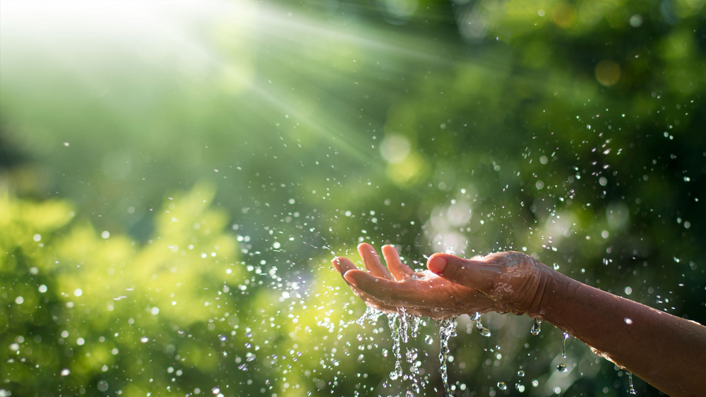 A hand with water splashing off it and the sun shining down