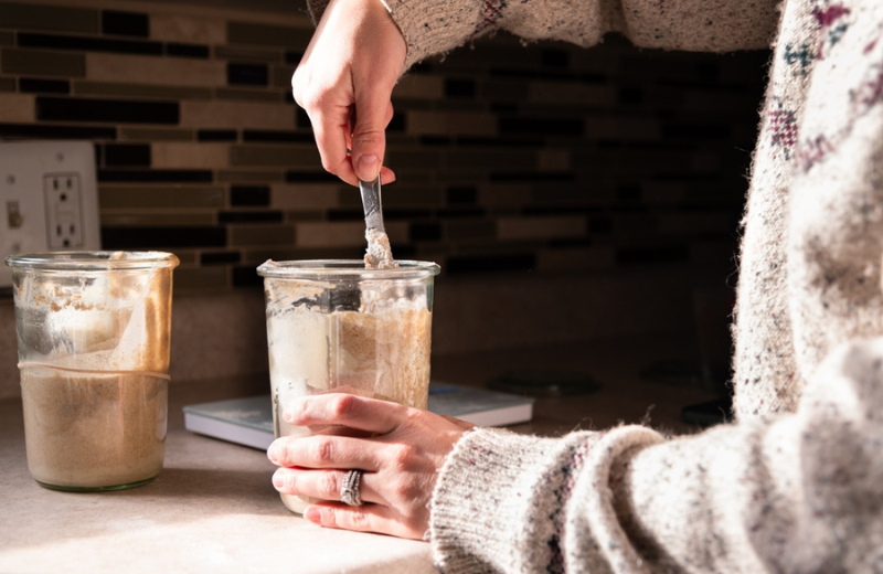 person holding a glass jar of sourdough starter
