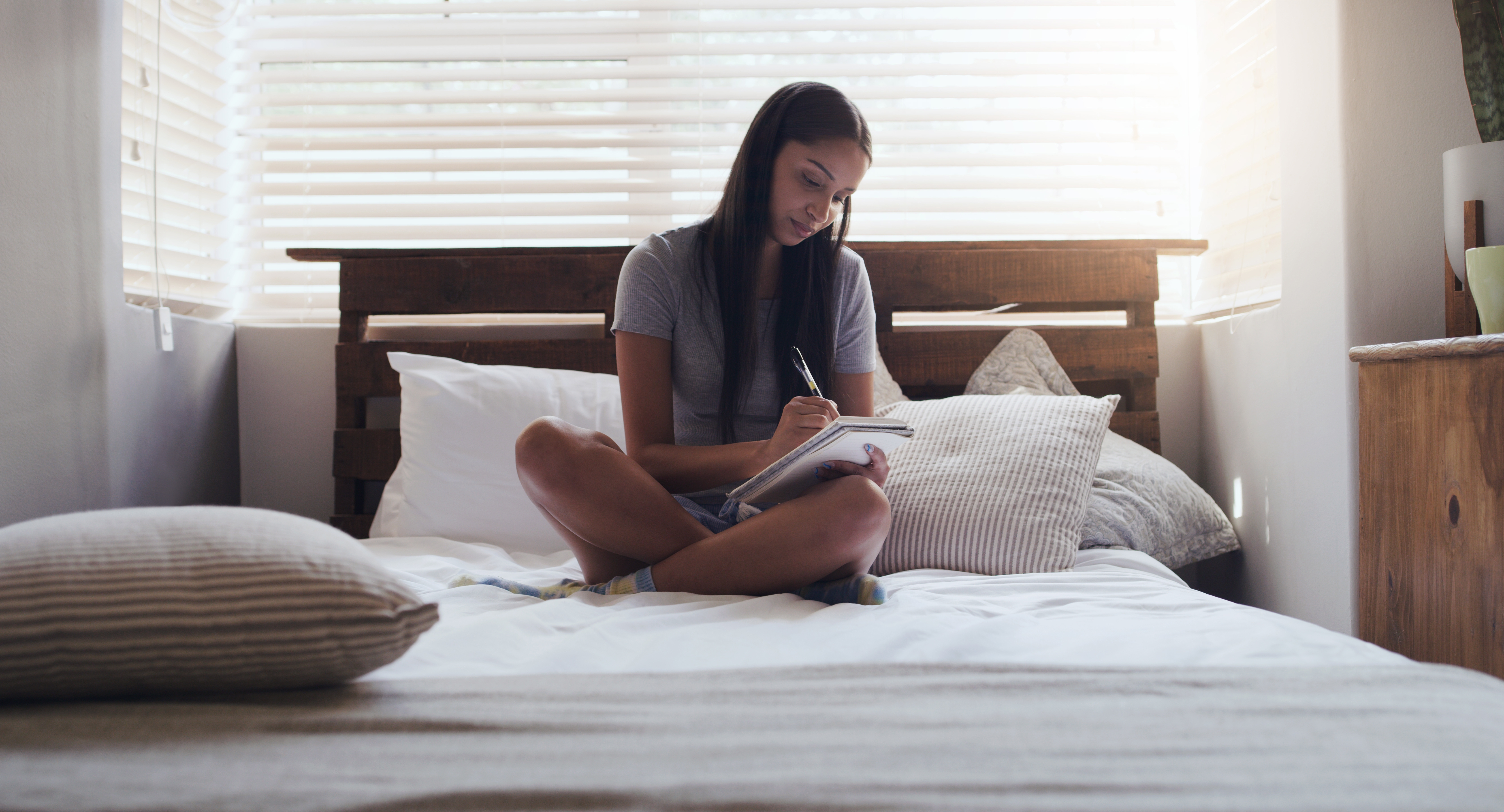 Someone sat cross legged on a bed, writing in a notebook