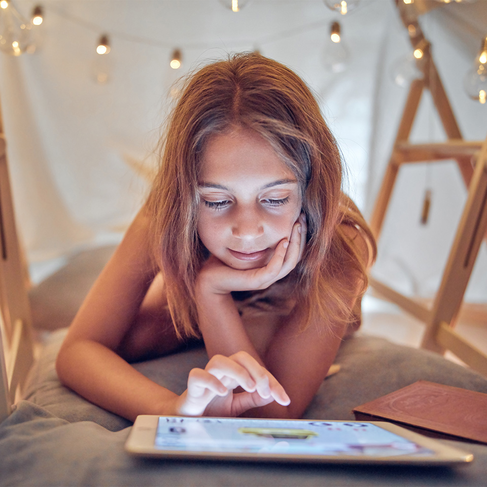 A child studying Year 6 English Course on a tablet under a home-made  indoor tent.