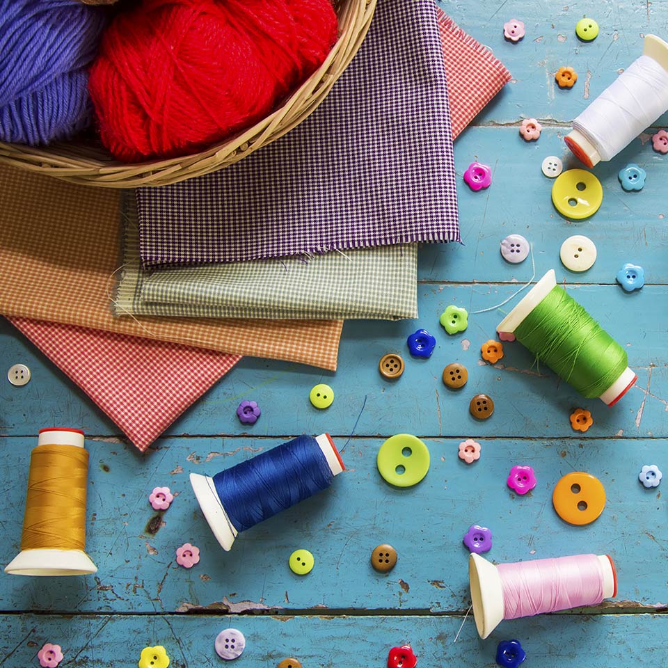 Cotton reels, wool, buttons, and fabrics strewn across a blue tabletop