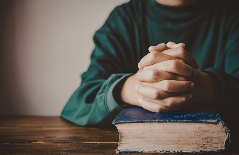 close up of hands praying above bible