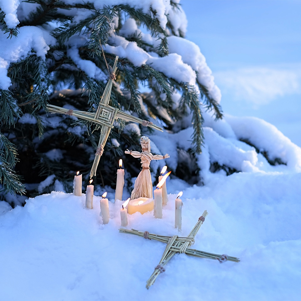 Brigid's cross of straw, candles, and doll on snow in a winter forest.