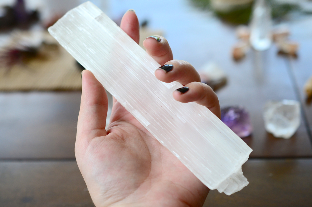 A hand holding a selenite rod.
