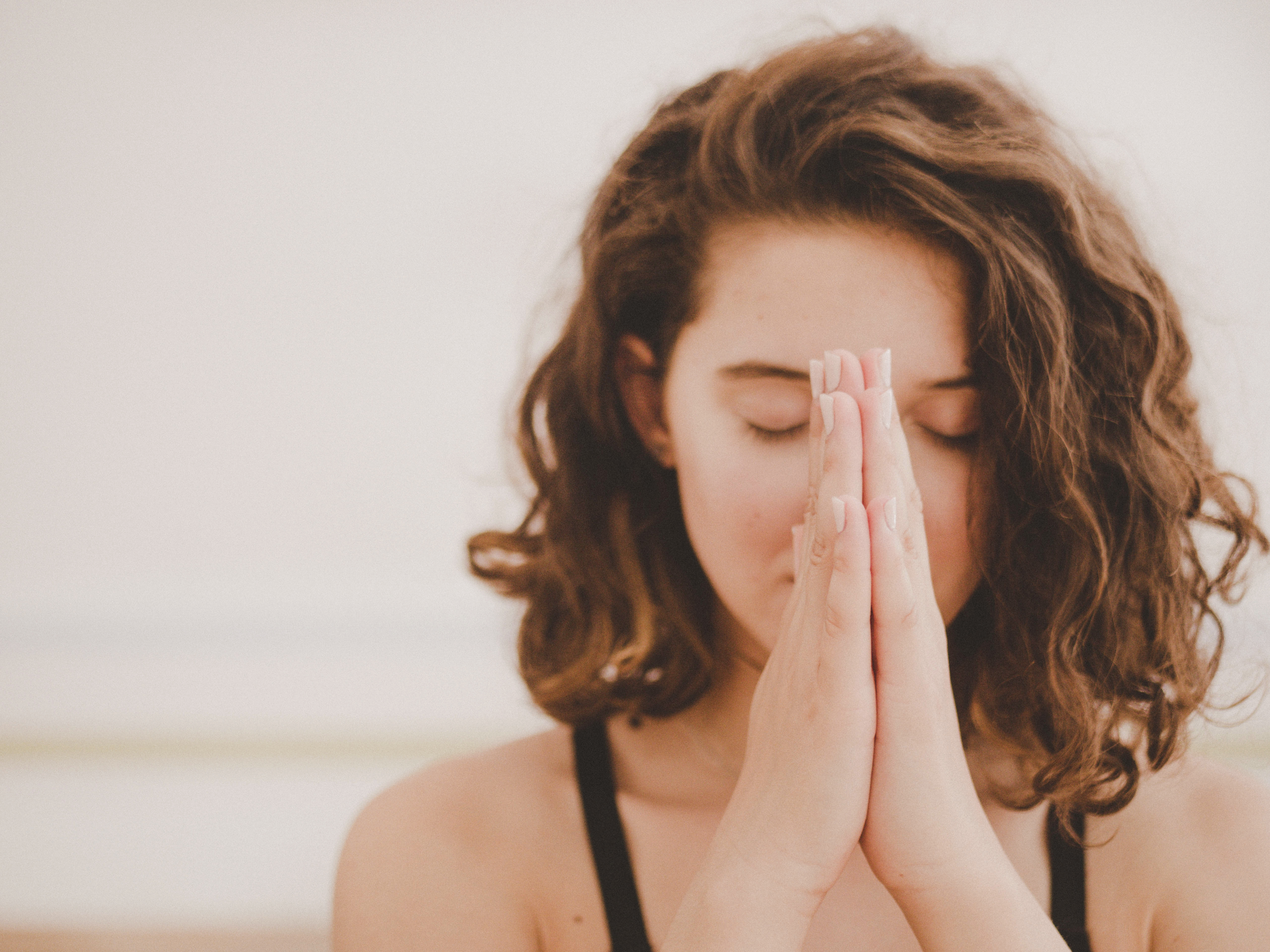 A woman with her eyes closed and her two palms pressed together in front of her face