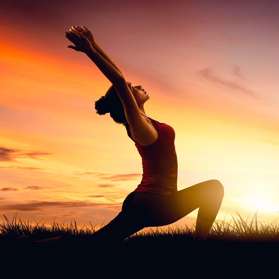 Woman practicing yoga warrior pose at sunset