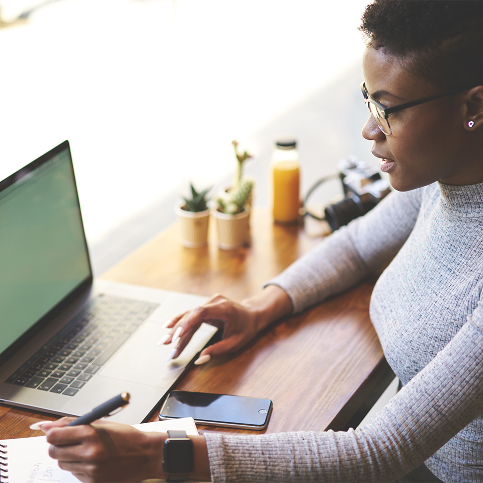 A copywriter working at a laptop and making notes with a notepad and pen