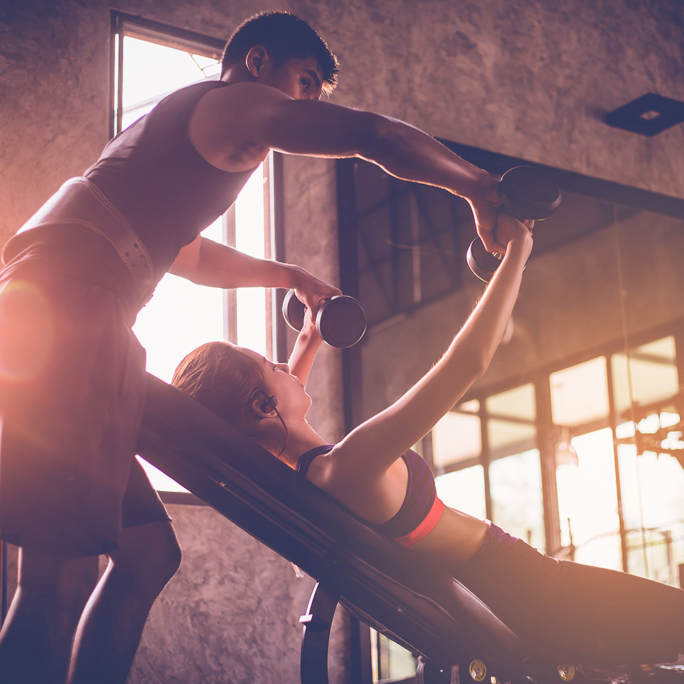 Woman doing weight exercises in a gym with the assistance of her personal trainer