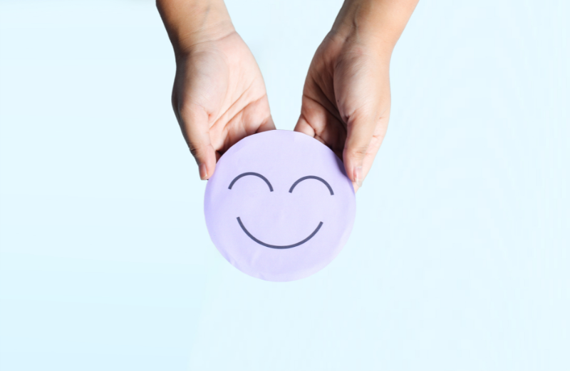 person holding purple smiling face to represent mental health