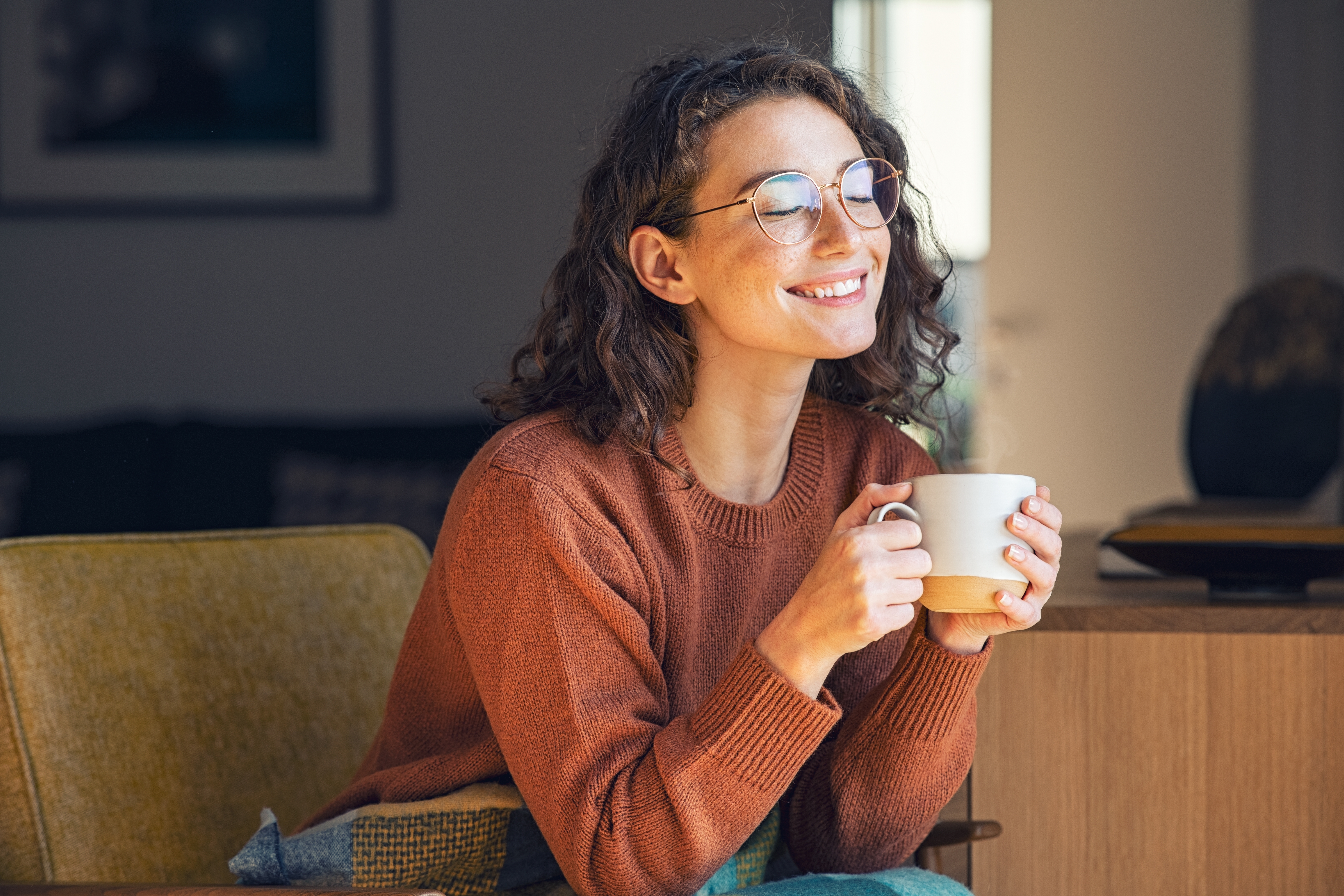 Woman in brown sweater smiling while holding cup of tea