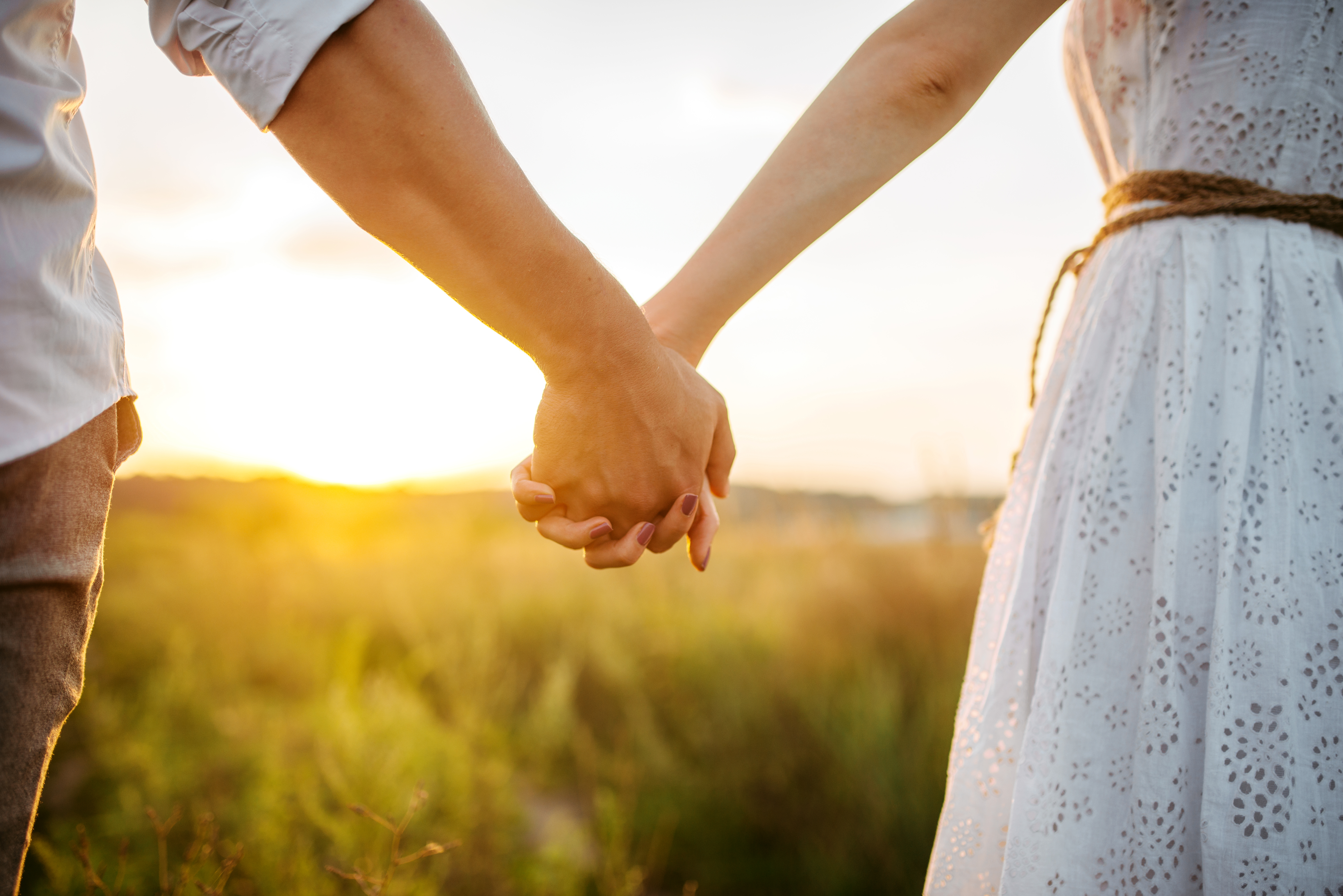 Couple holding hands in a field at sunset