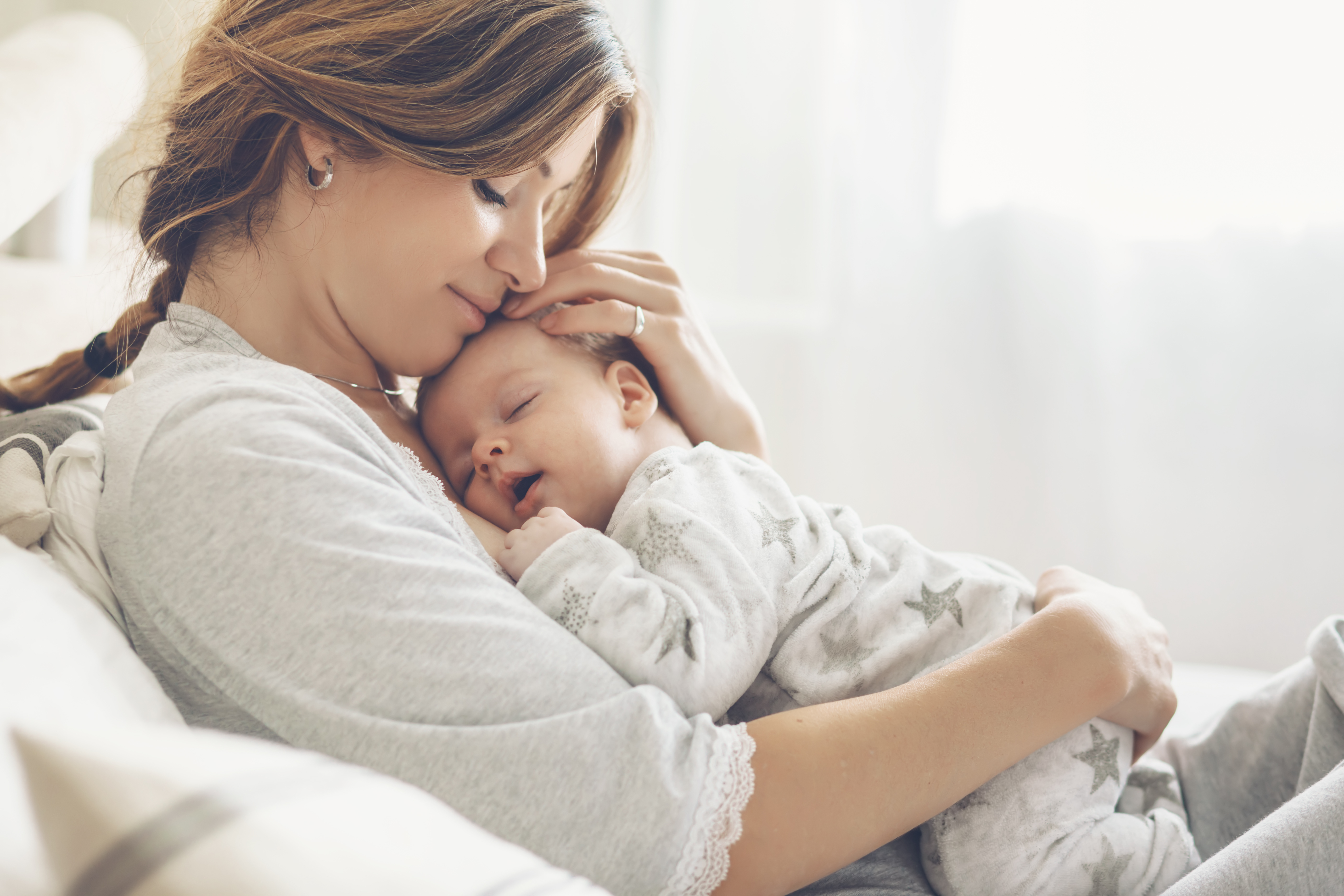 Woman cuddling baby in grey sleepsuit