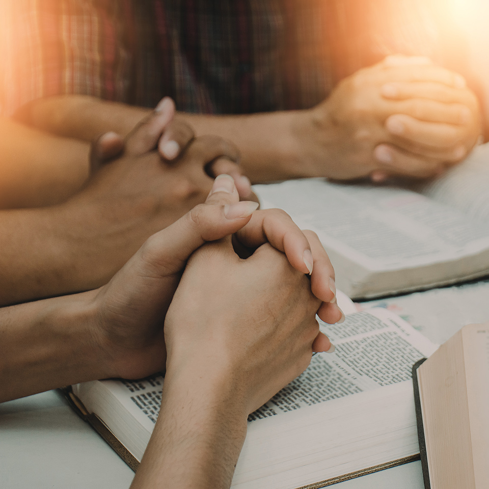 Hands held in prayer position resting upon open bibles