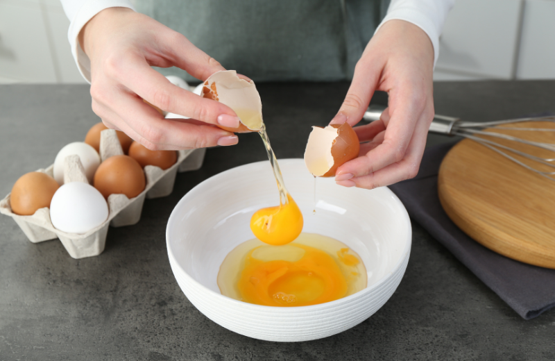 close up of a person cracking eggs into a bowl