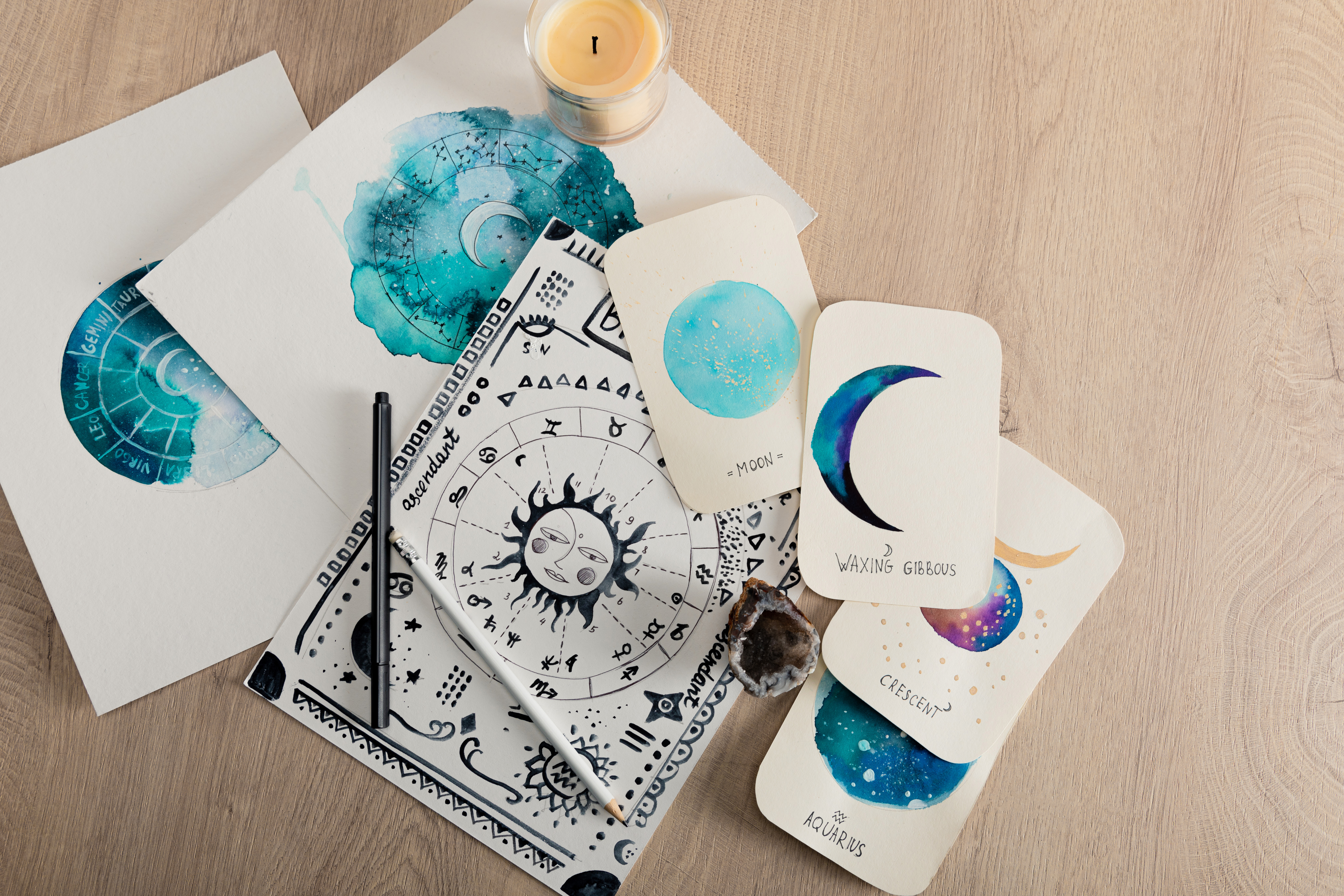 Top view of candle and cards with watercolor drawings of moon phases and zodiac signs on table