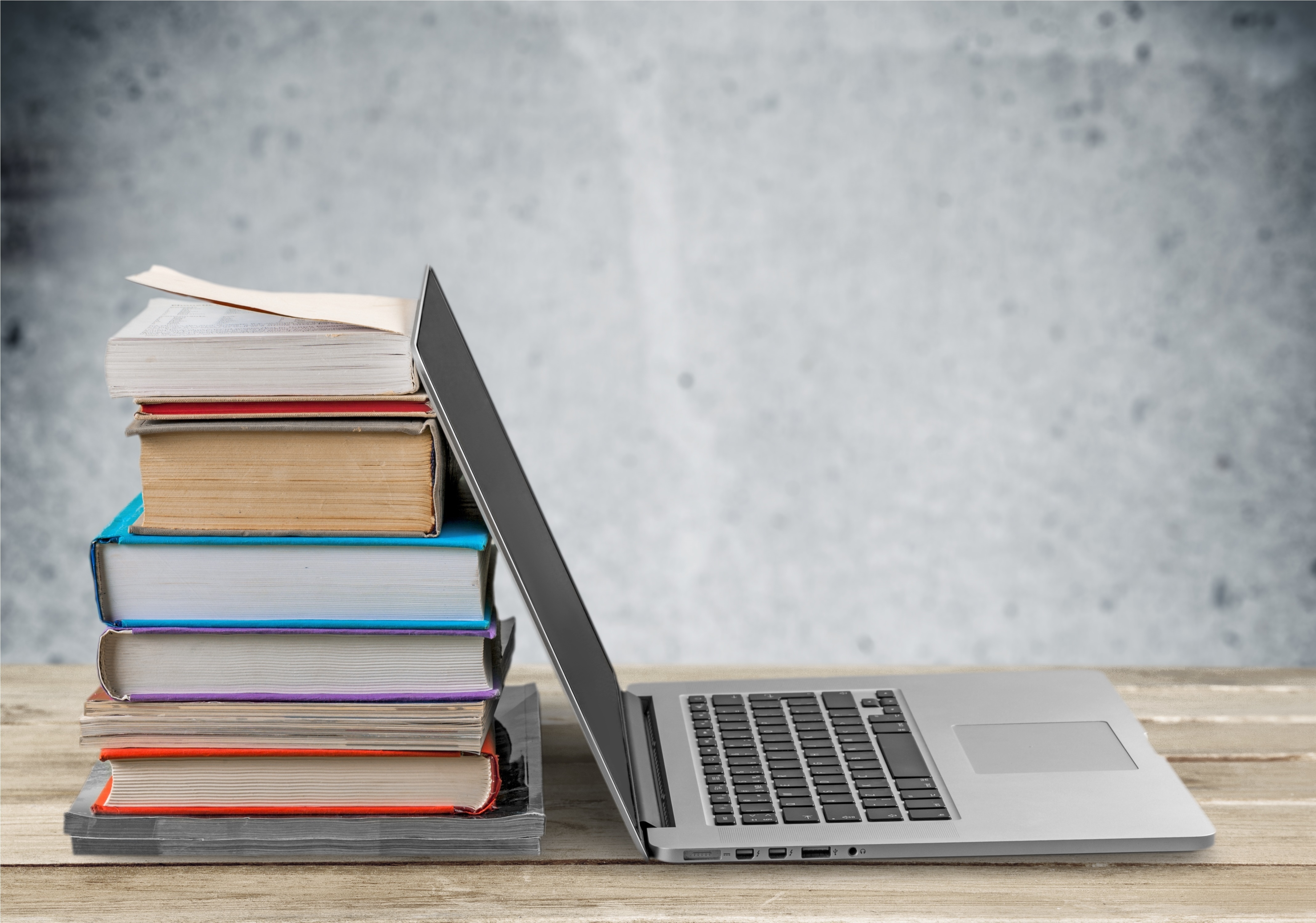 Books stacked next to laptop self publishing