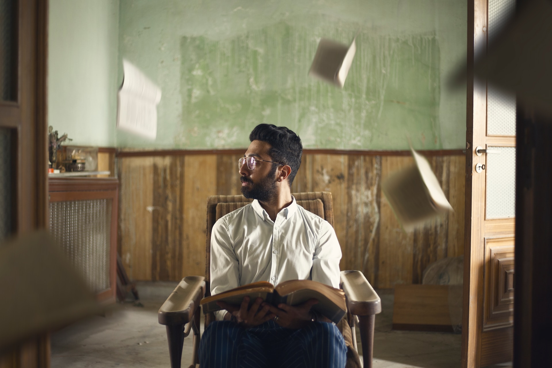 A man sitting in a chair with a book with books floating behind him