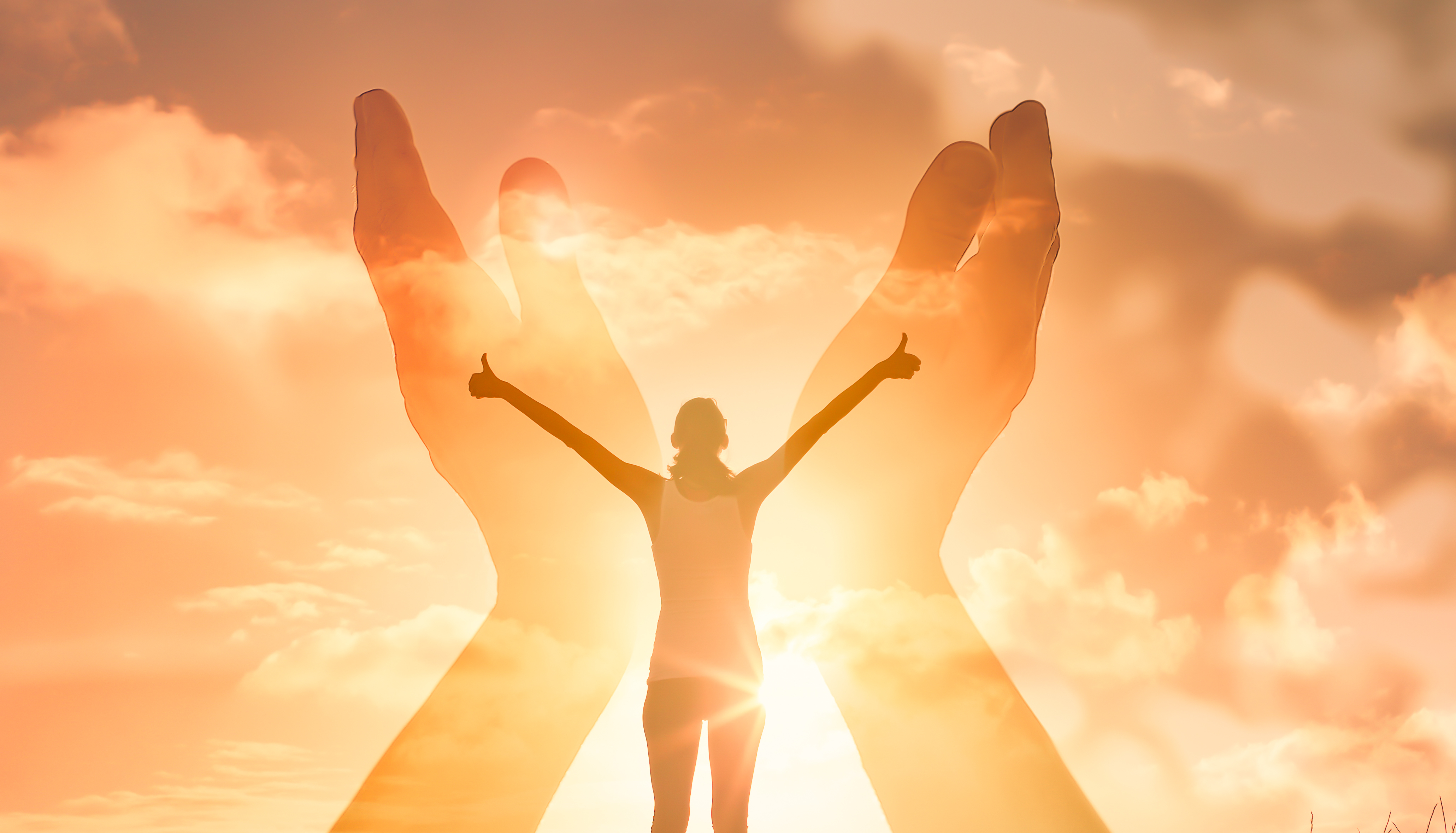 A woman stood in front of the sun with her arms up to the sky and thumbs up, with two large hands in front of her, with the palms up to the sky