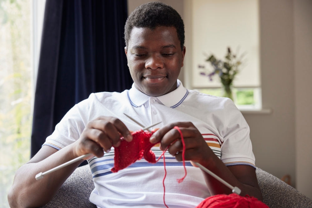 A black man knitting with red wool