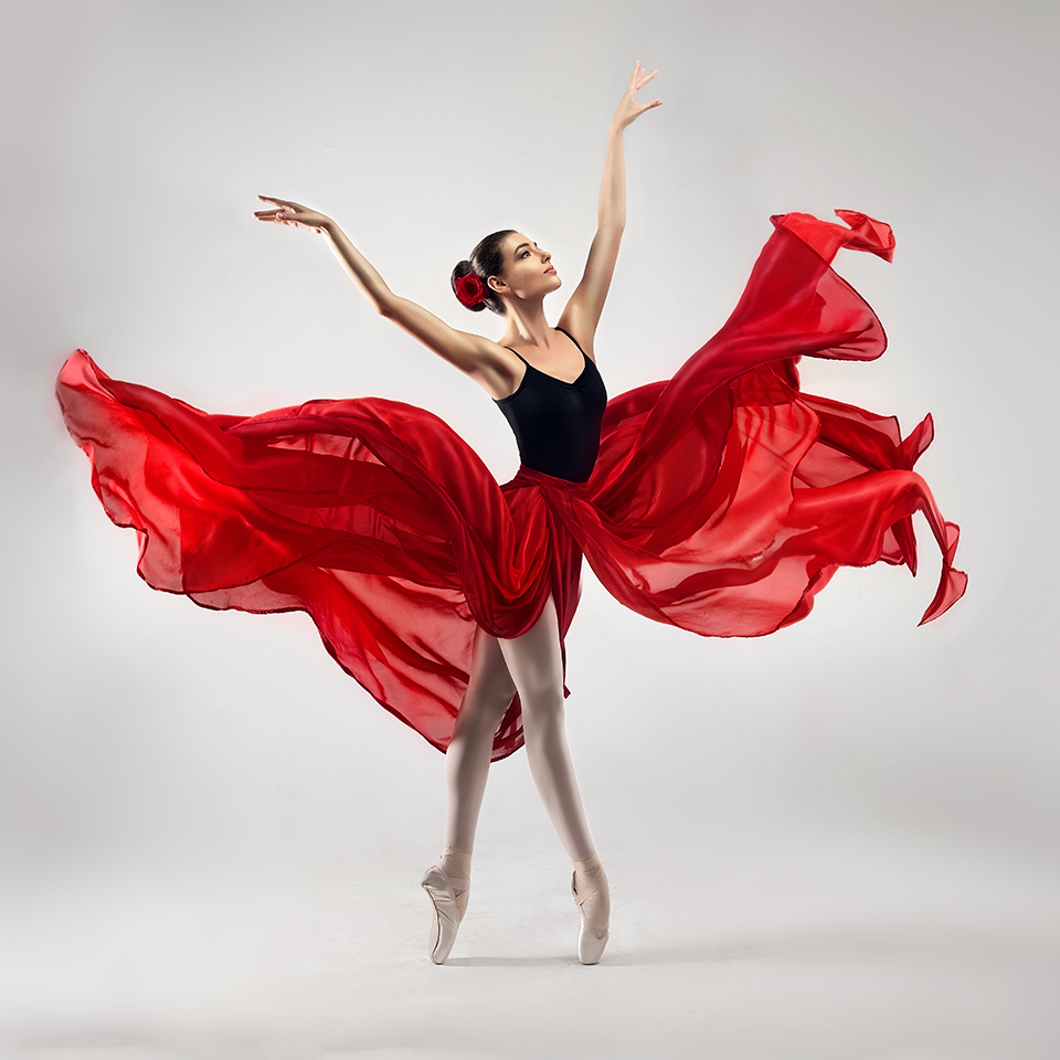 Ballet dancer, dressed in professional outfit, shoes and red weightless skirt in a ballet pose