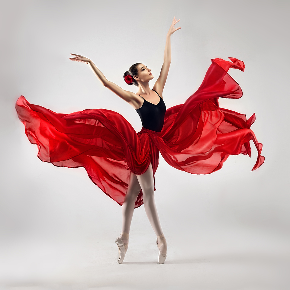 Ballet dancer, dressed in professional outfit, shoes and red weightless skirt in a ballet pose.