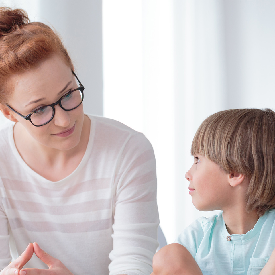 Young female school psychologist having serious conversation with smart little boy at her office