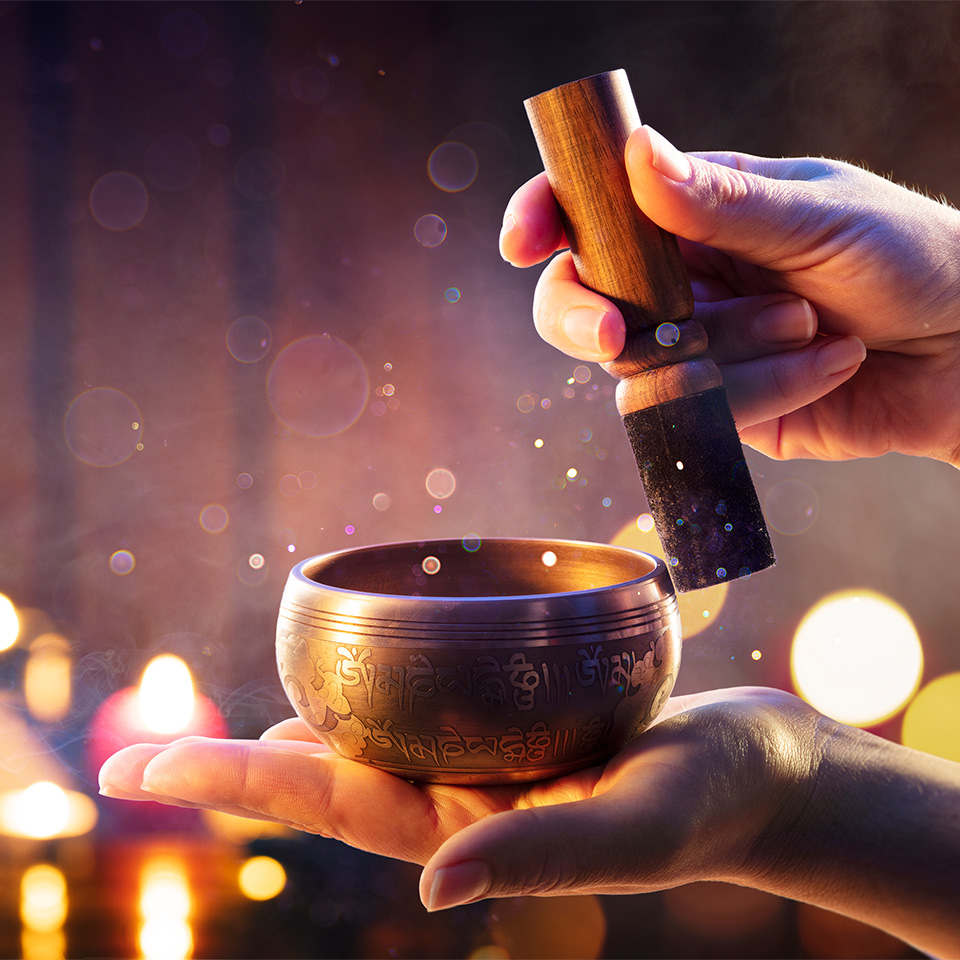 Tibetan singing bowl being used for sound healing on a background of lit candles